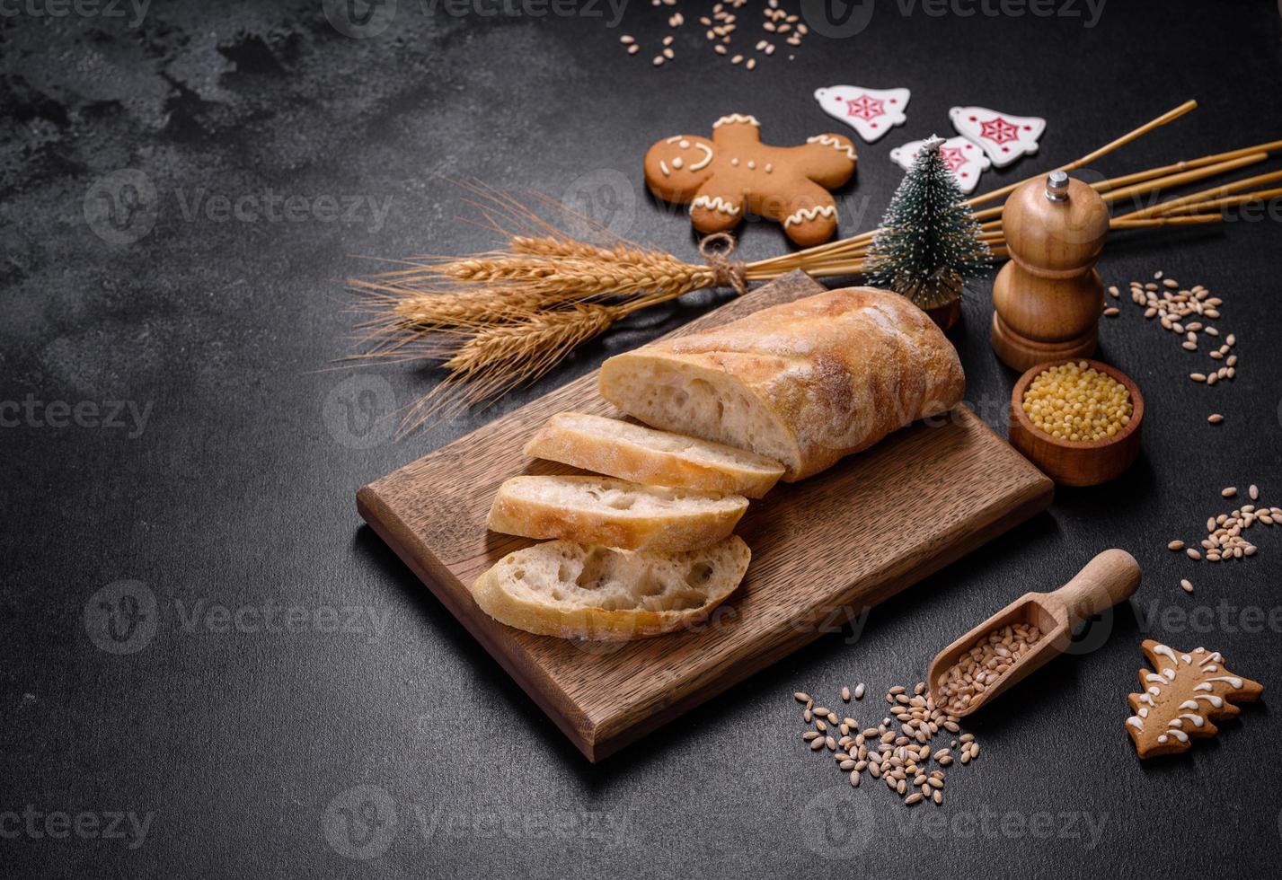 pan baguette francés cortado en una tabla de cortar de madera contra un fondo de hormigón oscuro foto