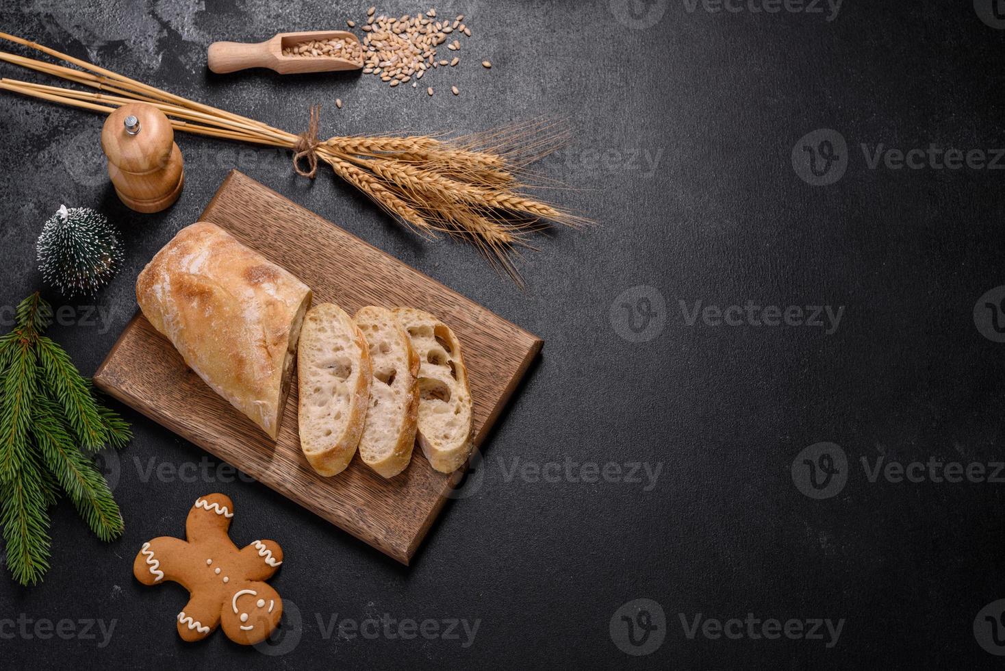 pan baguette francés cortado en una tabla de cortar de madera contra un fondo de hormigón oscuro foto