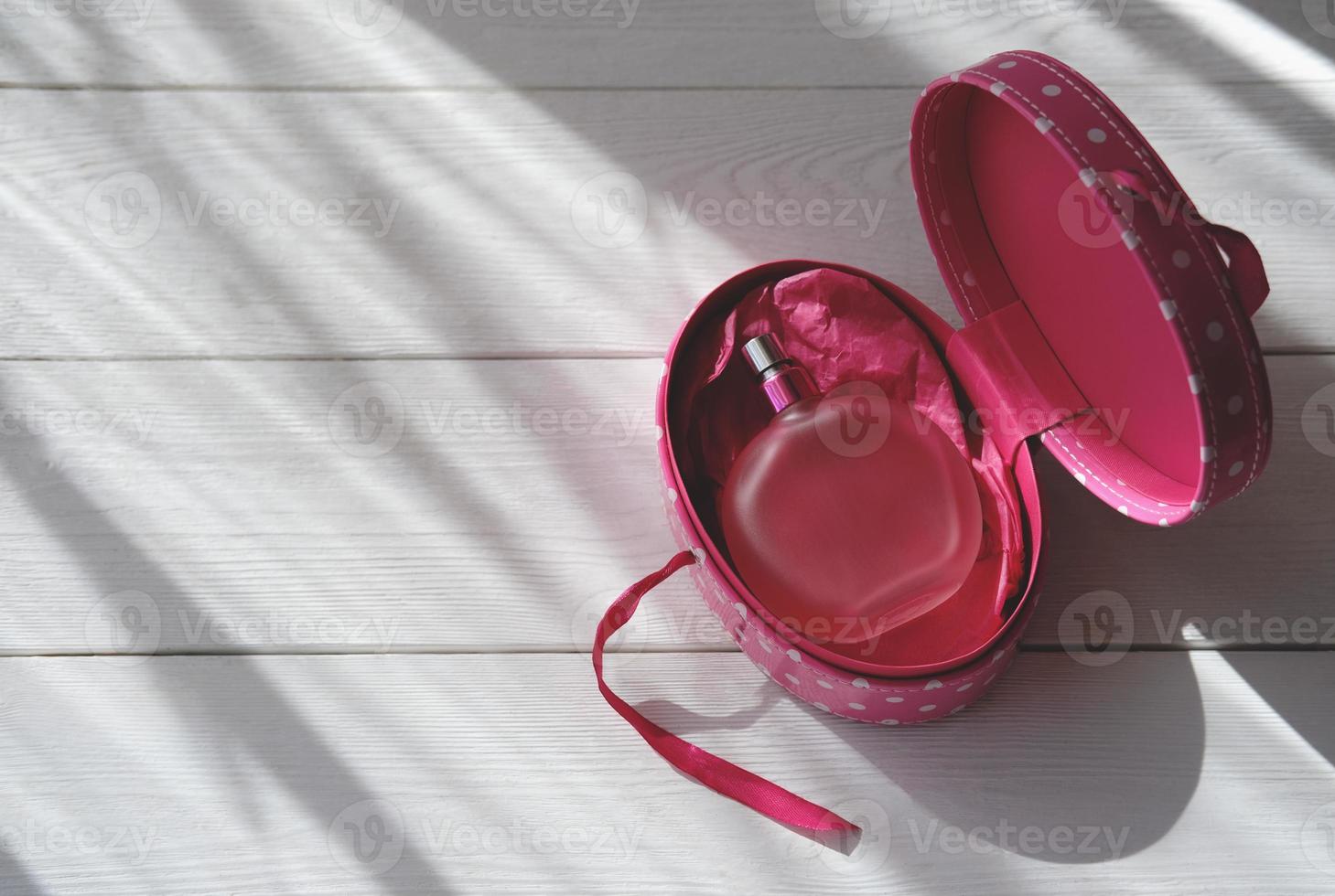 pink perfume bottle on white wooden background in direct light. photo