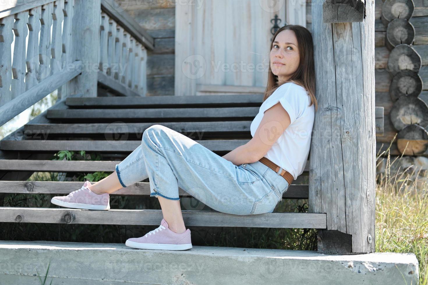 bonita mujer sentada en las escaleras de una vieja casa de madera abandonada. foto