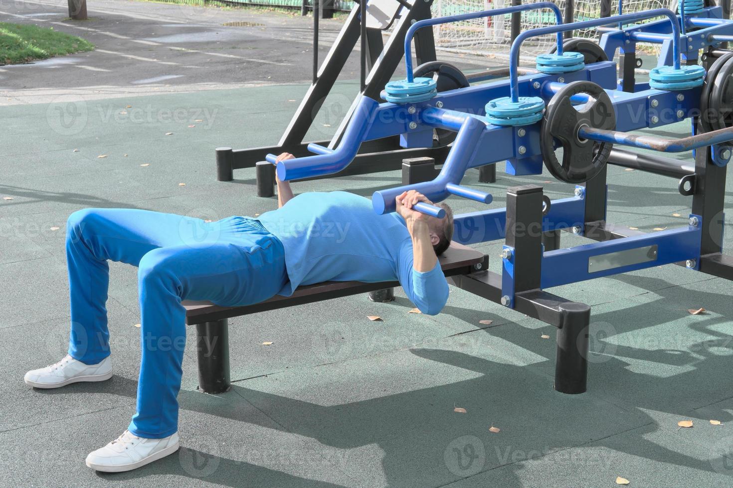 sporty slim man doing bench press using outdoors gym equipment. photo