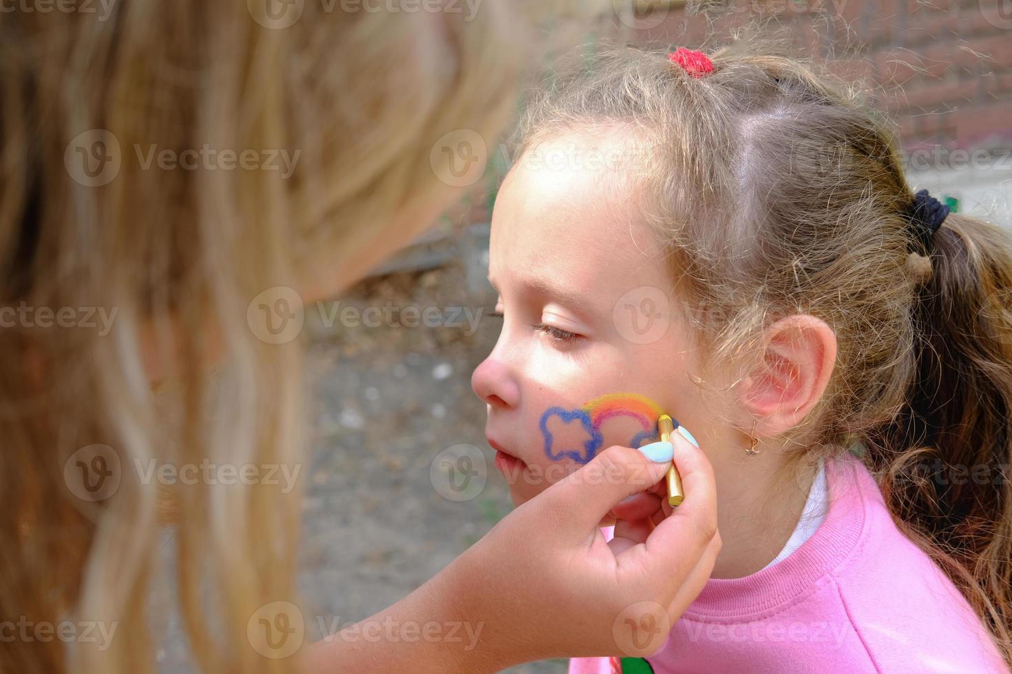 Artist painting a rainbow on girl's face. photo