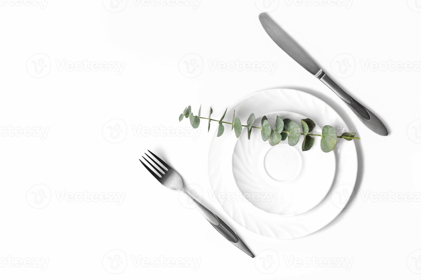 Spring elegant table setting, restaurant menu concept. white dishes and silverware and eucaliptus branches on a table. mock up for meal placement. top view, flat lay photo