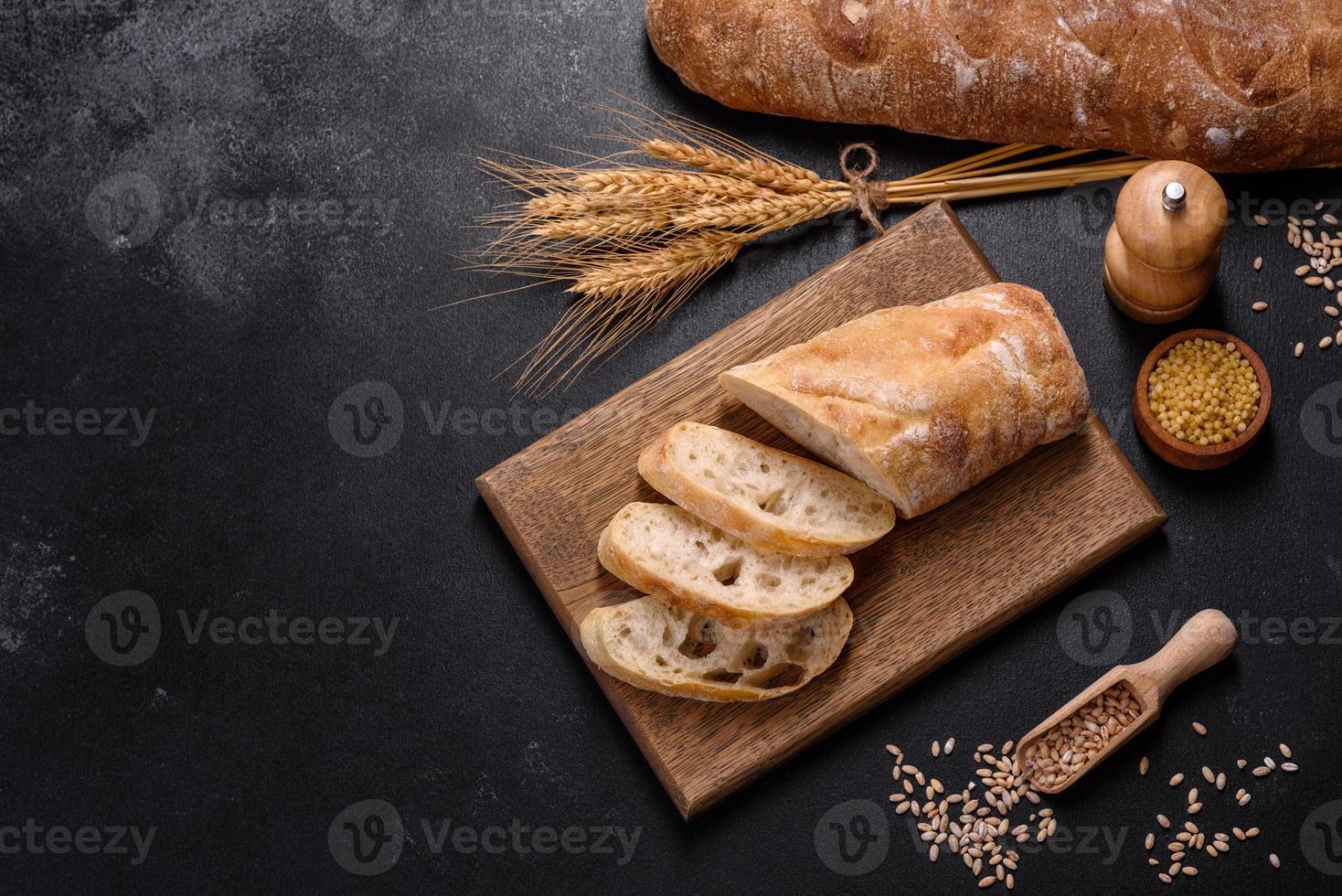 French baguette bread sliced on a wooden cutting board against a dark concrete background photo