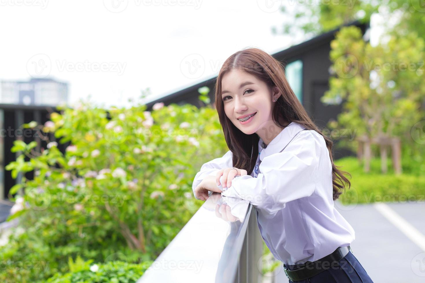 una joven asiática con uniforme escolar sonríe con frenos en los dientes en un parque en el centro de la ciudad. foto