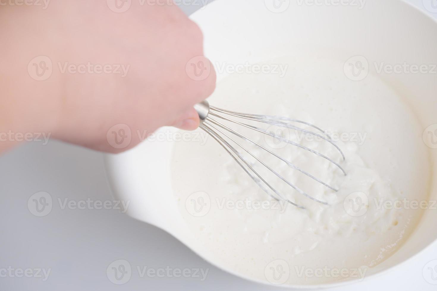 mano sosteniendo un batidor y mezclando un postre de panna cotta. foto