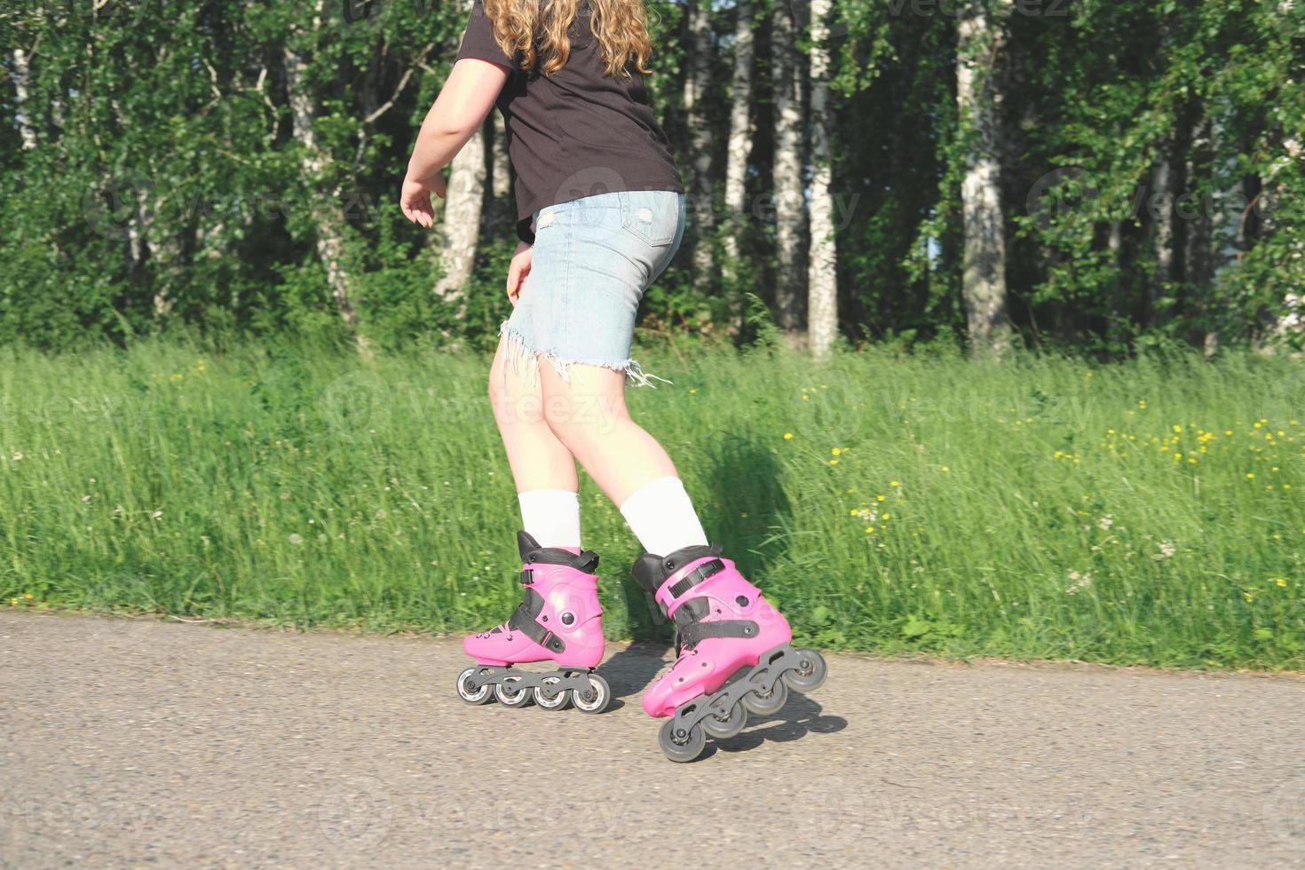 teenager girl practicing in rollerskating in a summer park. partial view. pink inline rollers. teen leisure and sports photo