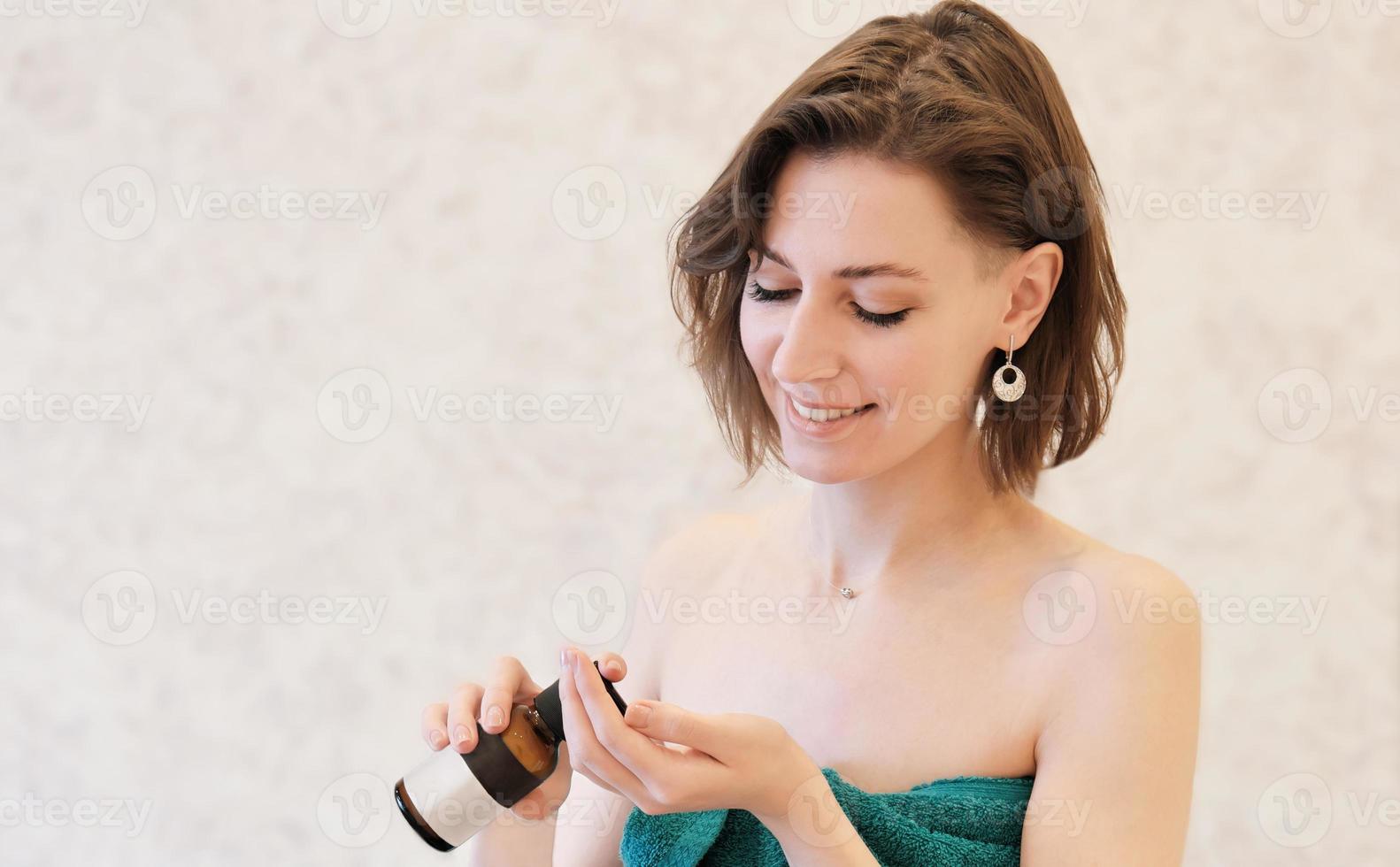 mujer joven que usa loción cosmética o crema. producto de cuidado corporal para una piel perfecta. mujer con toalla de baño y aplicando humectante. botella cosmética de belleza sin marca foto
