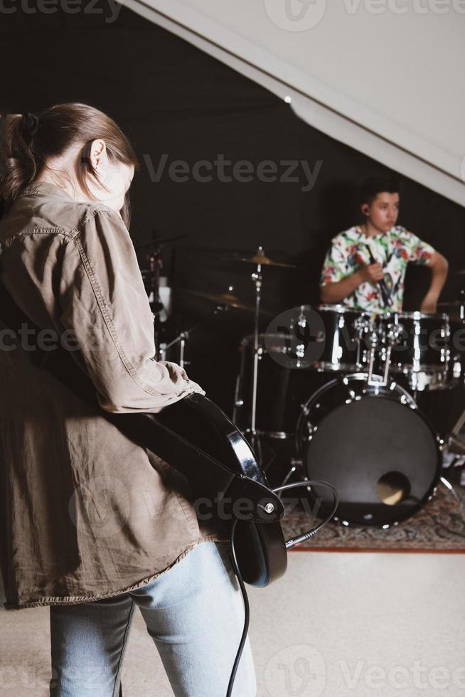 rock band rehearsal in a studio. female bass guitarist and teen male drummer performing a song. vertical size photo