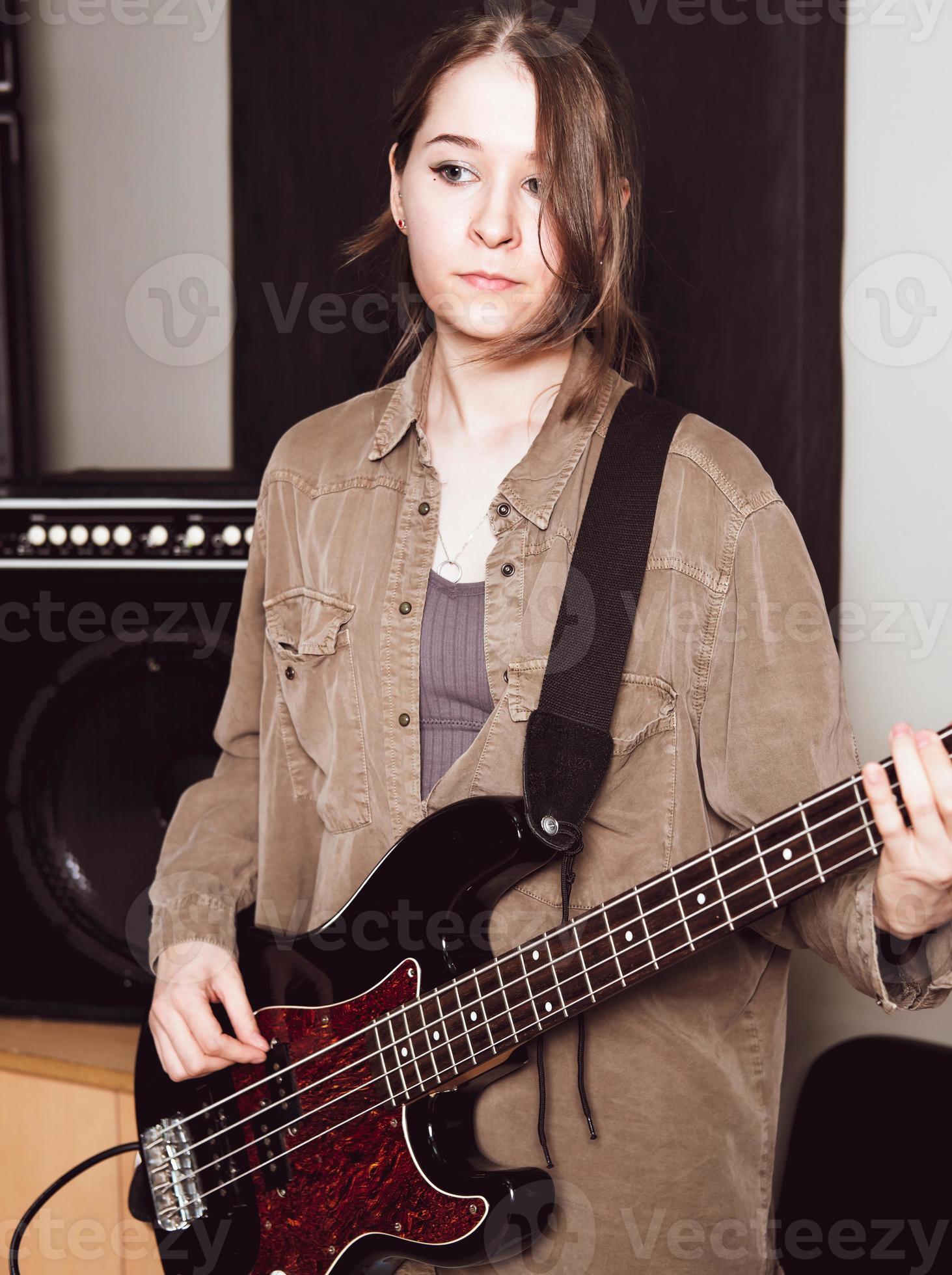 young woman wearing casual clothes and playing electric bass guitar looking  aside. female bass guitarist standing in a rehearsal room 8384149 Stock  Photo at Vecteezy