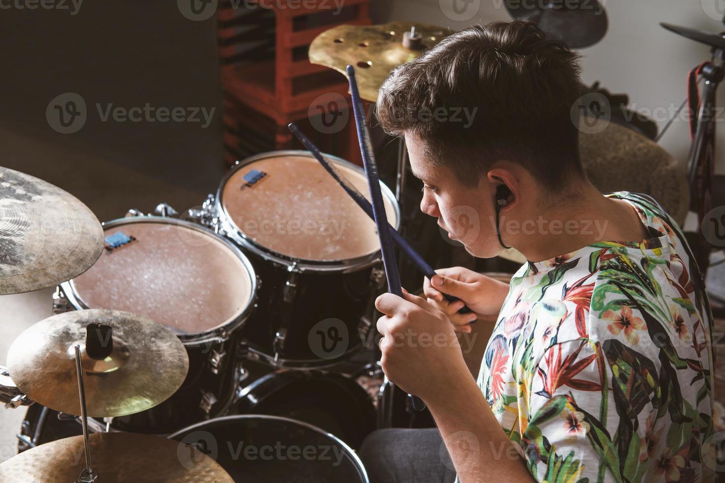 teenager boy drummer playing on rehearsal in a studio. rock musician male teen performing a song. rear view photo