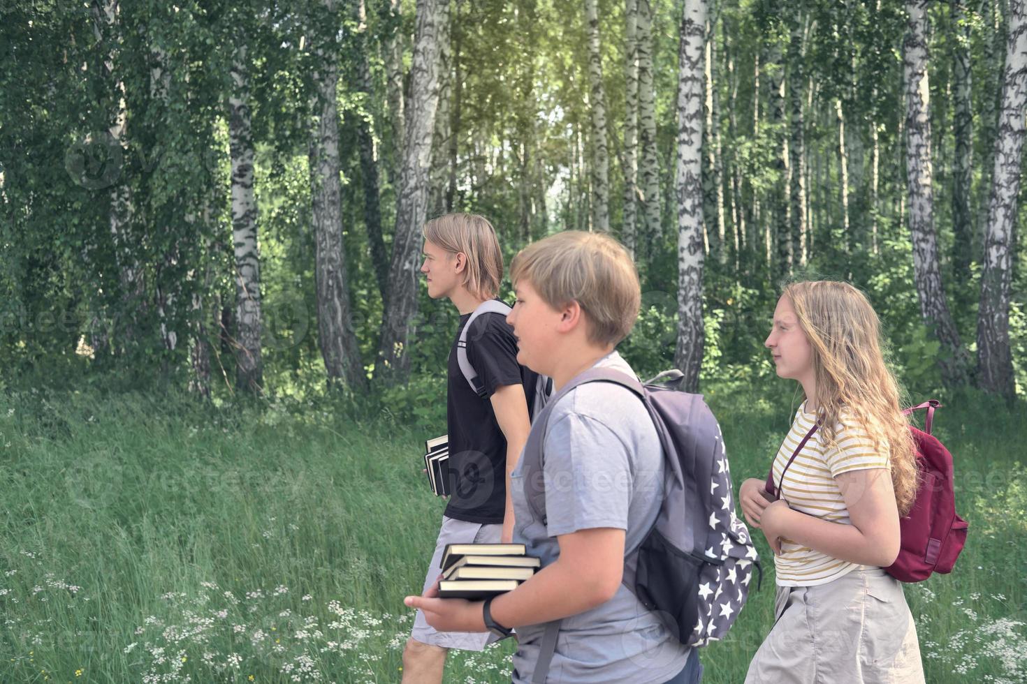 group of teenagers go to school through the park with backpacks and books. back to school concept. side view, caucasian teens, side view. blond hair. photo