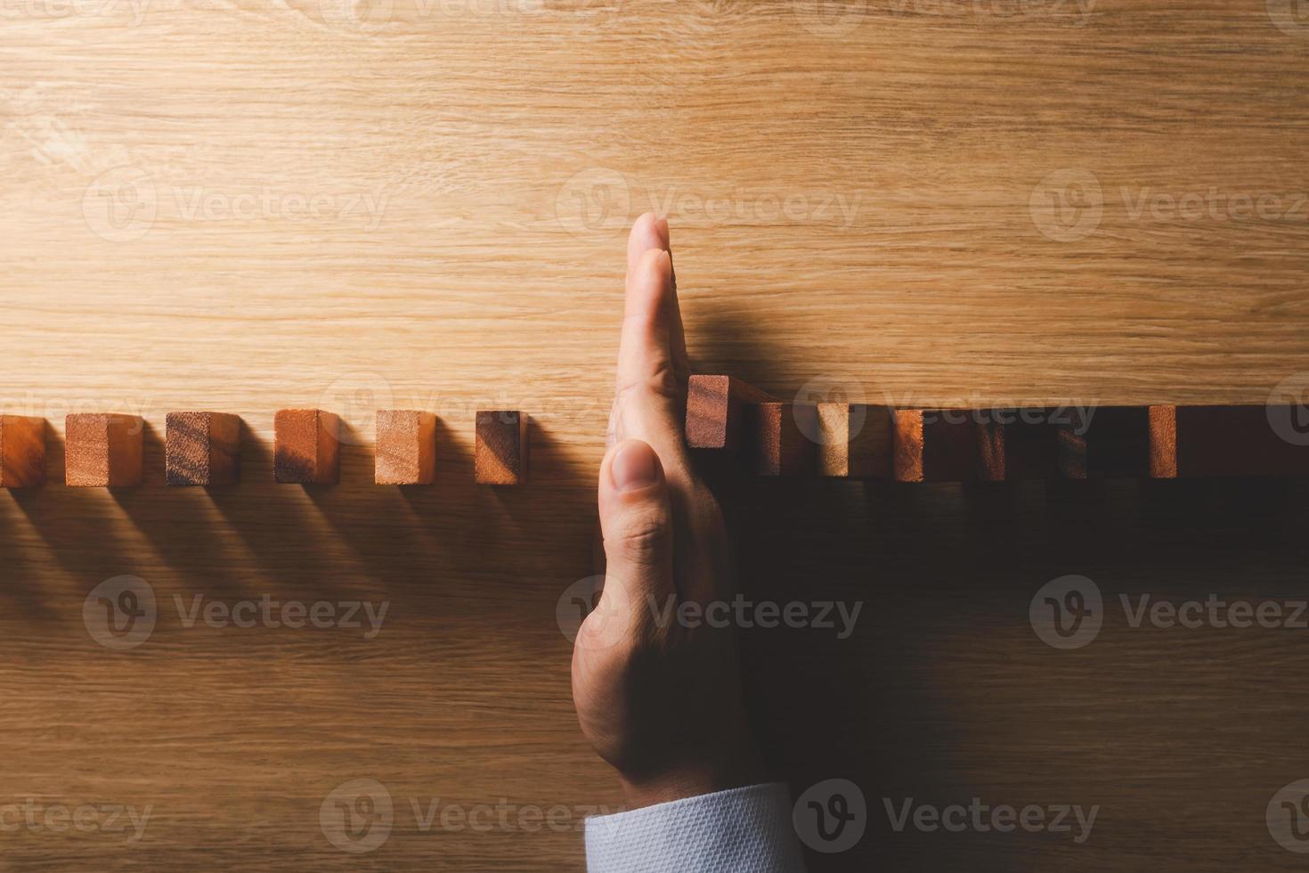 Risk management and business strategy concept, businessman hands stop the dominoes from falling continuously, preventing future risks from crisis. photo