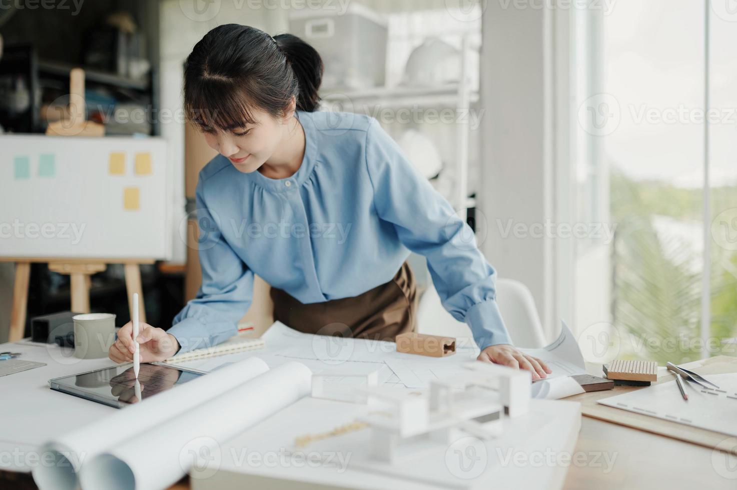 enfoque selectivo, arquitecta o ingeniera asiática dibujando el diseño del interior del edificio usando una tableta. una arquitecta o ingeniera asiática se sienta y analiza, diseña proyectos en la oficina. foto