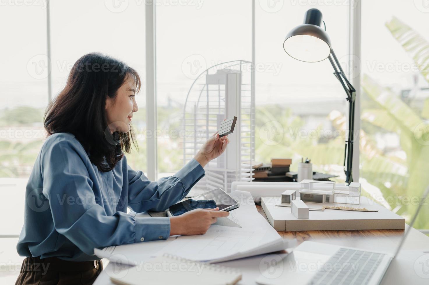 enfoque selectivo, arquitecta o ingeniera asiática que actualmente considera materiales para diseñar condominios modernos. arquitecta o ingeniera asiática sentada y analizando, diseñando proyectos en la oficina foto