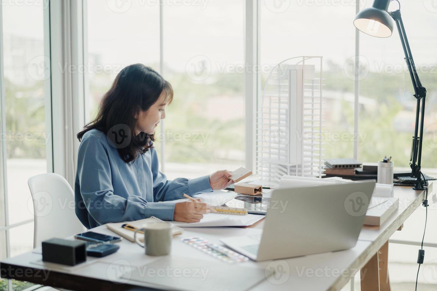 enfoque selectivo, arquitecta o ingeniera asiática que actualmente considera materiales para diseñar condominios modernos. arquitecta o ingeniera asiática sentada y analizando, diseñando proyectos en la oficina foto