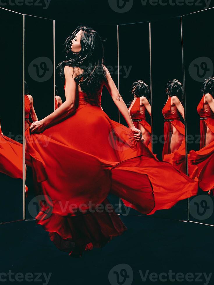Portrait of beautiful brunette woman in red shoes and dress turning around and dancing near the mirrors photo