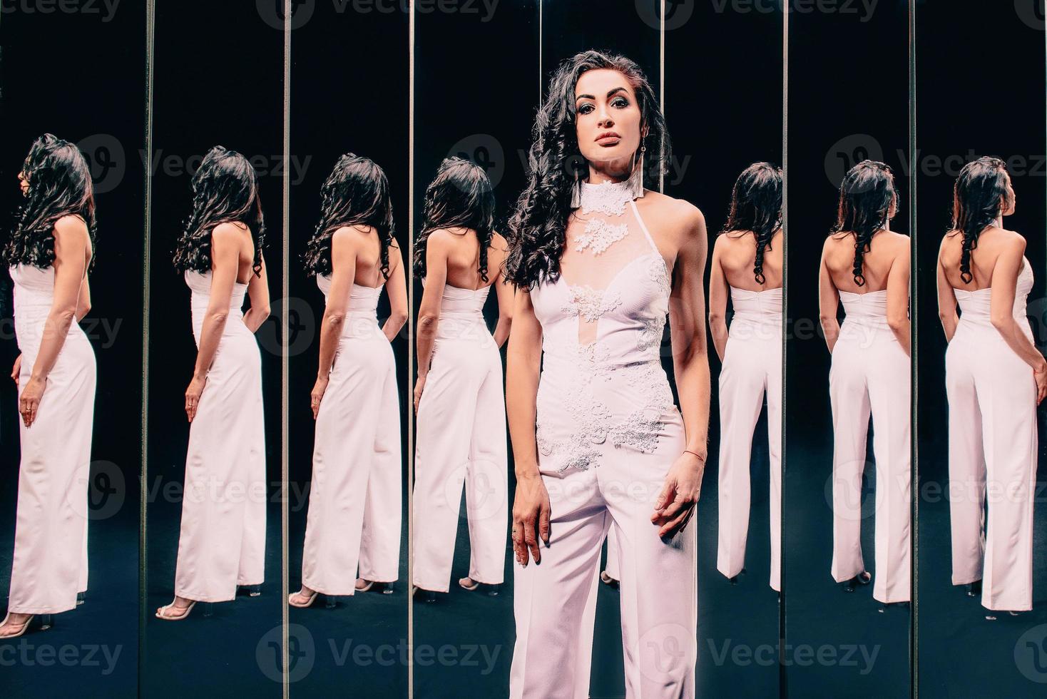 Portrait of beautiful brunette woman in white shoes and white pants suit standing near the mirrors photo