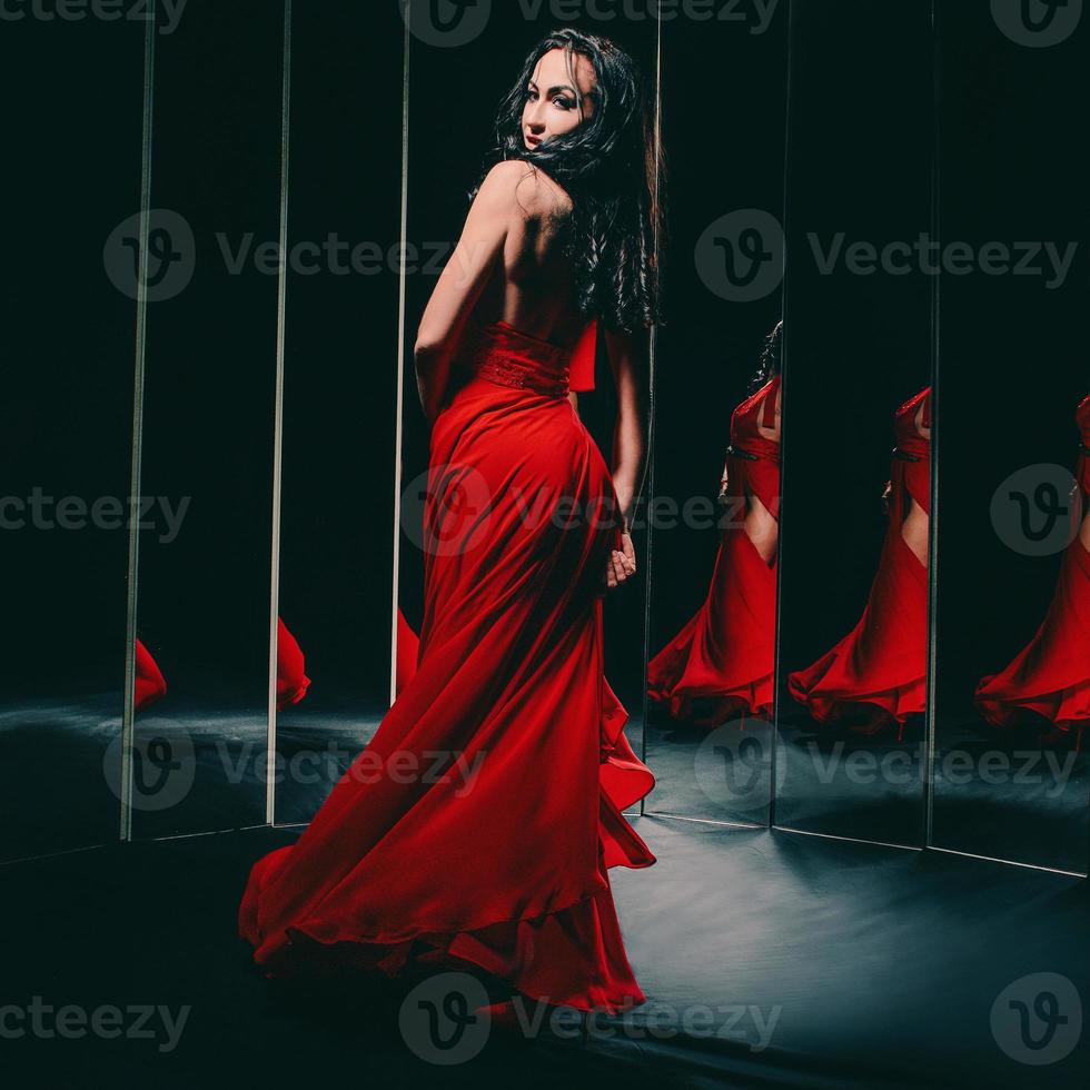 Portrait of beautiful brunette woman in red shoes and dress turning around and dancing near the mirrors photo