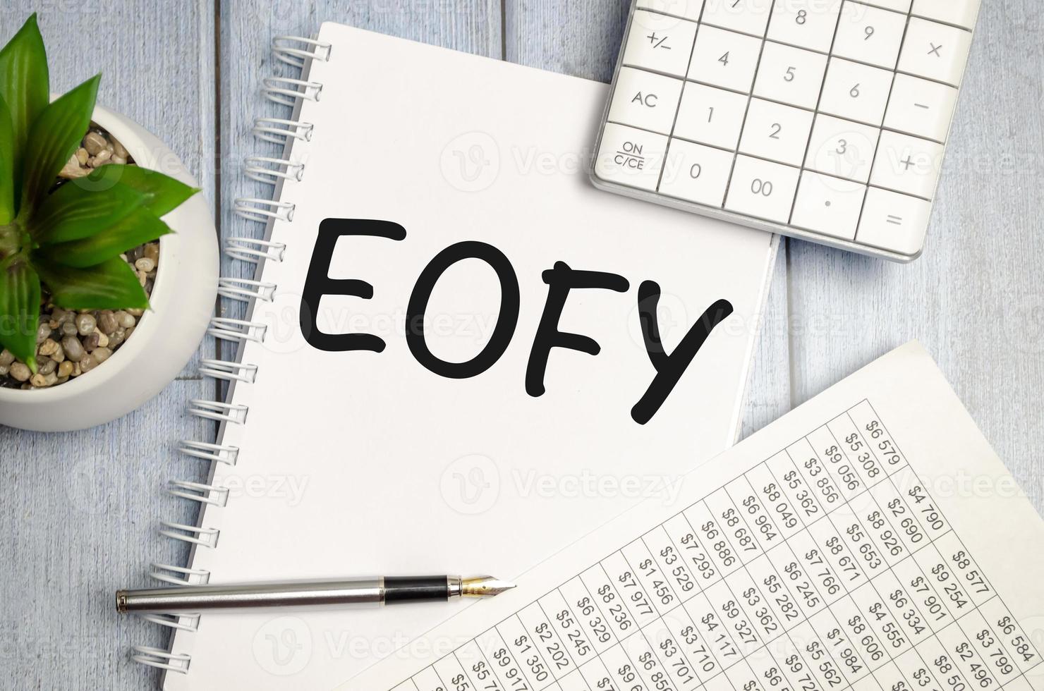 notebook over wood table background, focus on wooden blocks with letters making End of Financial Year text photo
