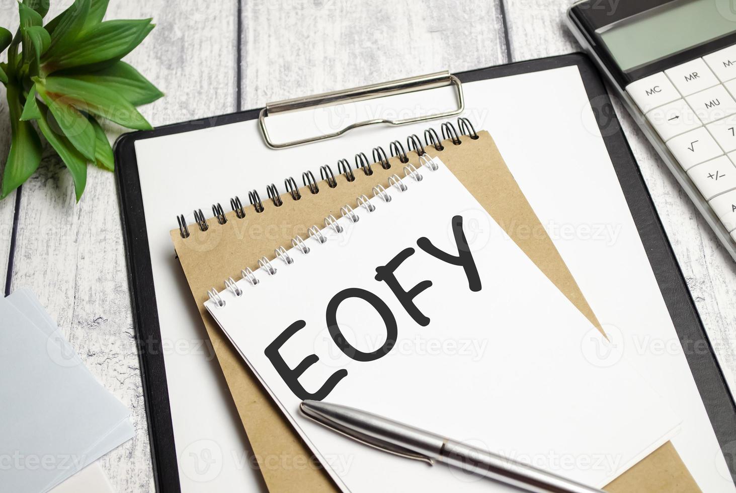 notebook over wood table background, focus on wooden blocks with letters making End of Financial Year text photo