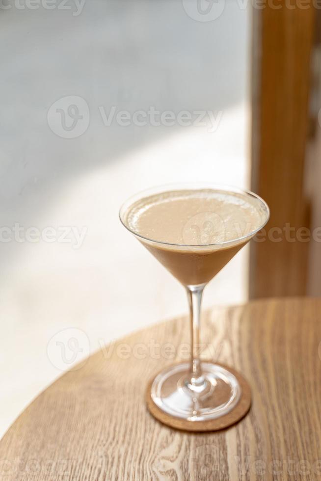 Fresh stylish latte coffee cocktail in Martini glass on the wooden table on side window with natural sunlight at cafe. photo