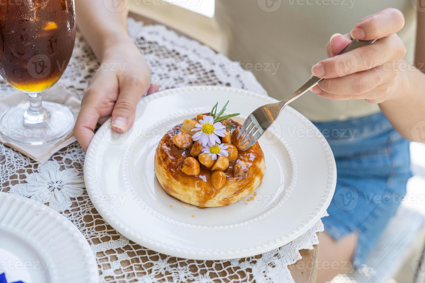 woman hand used fork eat Homemade puff pastry deep fried donuts or cronuts. croissant and doughnut topping with macadamia nut and caramel sauce. photo