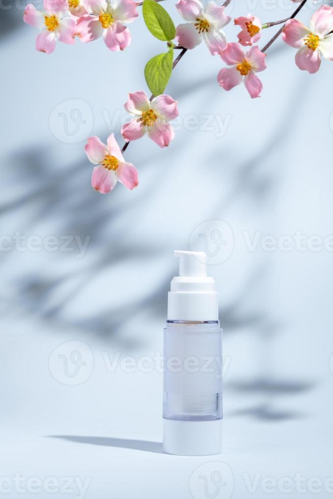 paquete cosmético y de cuidado de la piel en una botella de vidrio sobre fondo blanco con flores y sombras duras o duras y luz solar de la rama del árbol de hojas cayendo sobre la pared. diseño de productos de belleza moderno y minimalista. foto