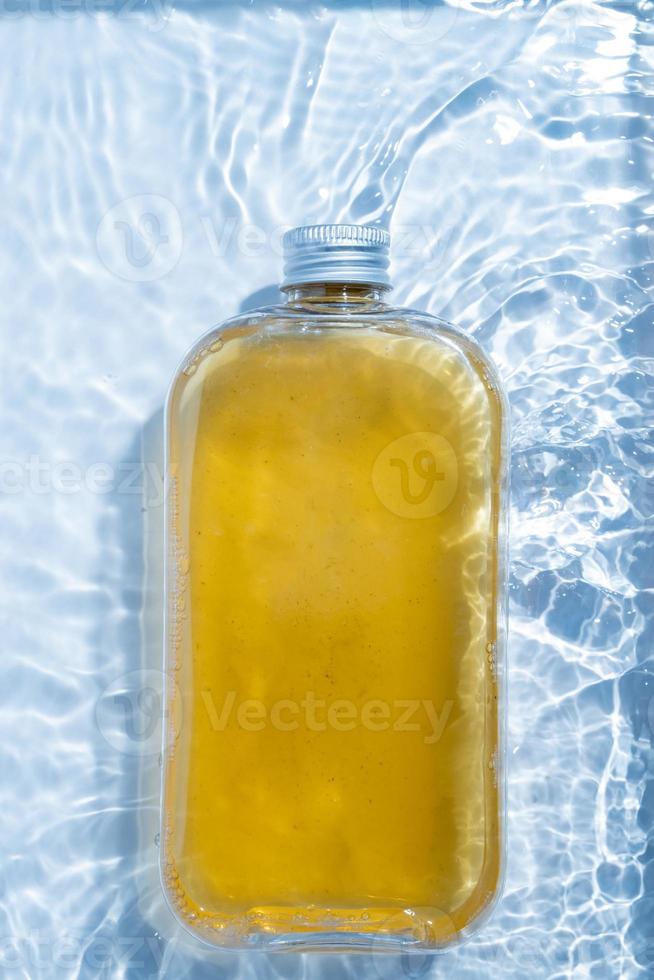 A plastic drink cold clear bottle is placed in the water pool. Transparent blue colored clear water surface texture with ripples, splashes and bubbles nature background Water waves in sunlight photo