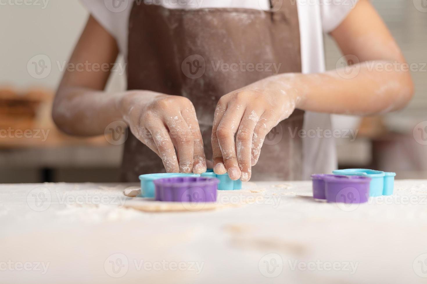 una niña con un delantal marrón está usando un molde azul para cortar la masa foto