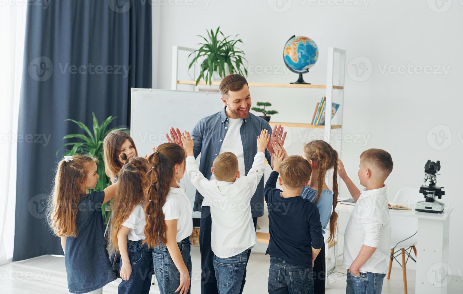 de pie y chocando los cinco. grupo de niños estudiantes en clase en la escuela con el maestro foto