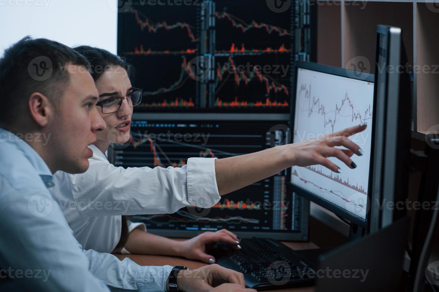 Looks like we must achieve that line. Team of stockbrokers are having a conversation in a office with multiple display screens photo