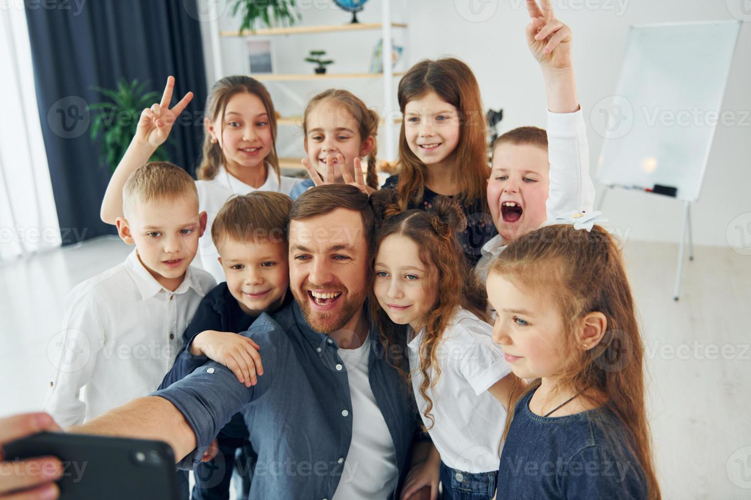 haciendo un selfie por teléfono. grupo de niños estudiantes en clase en la escuela con el maestro foto