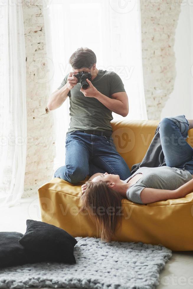 Backstage conception. Photographer taking a shot of young girl that lying on the white sofa photo