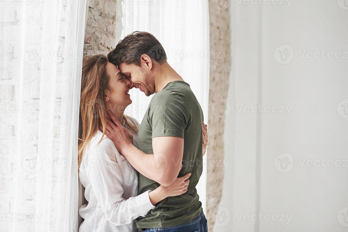 Attractive youth. Lovely couple kissing and enjoying each other near the window of their new home photo