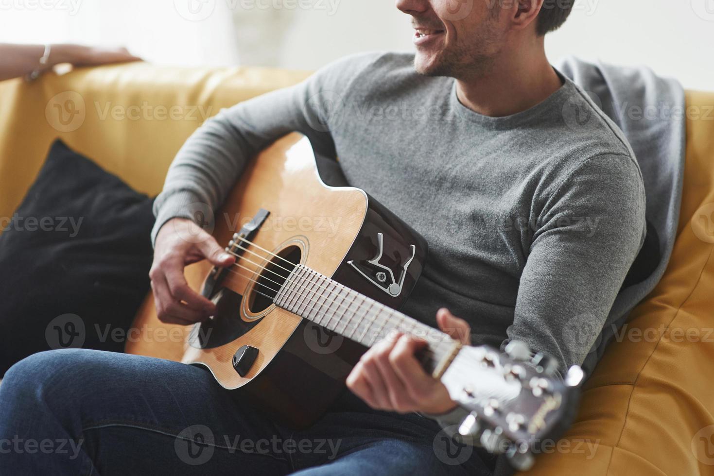 Man with acoustic guitar playing when sitting on the yellow sofa photo