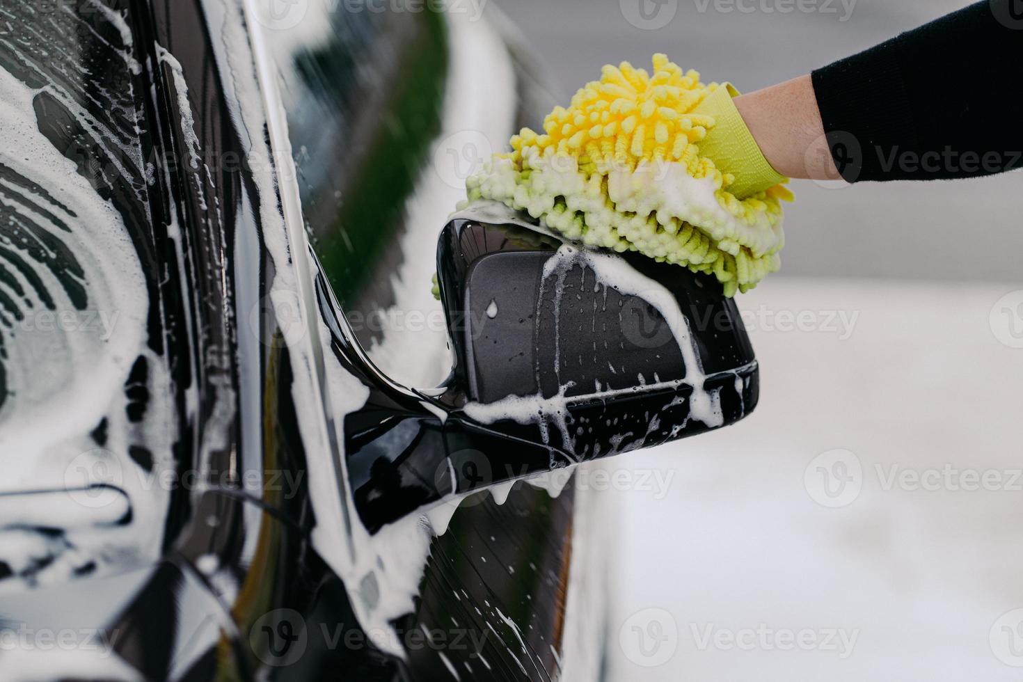 mans mano sujetando una esponja para lavar el coche. auto negro