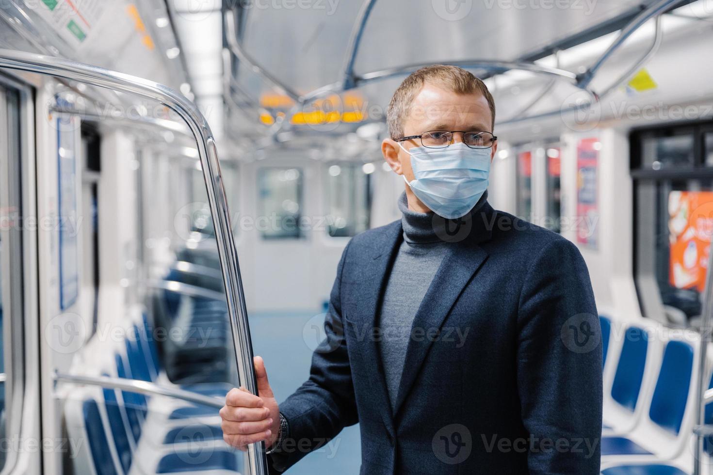 Male commuter poses in empty subway carriage, wears medical mask to prevent infected coronavirus at public metro station, looks somewhere, thinks about social distancing. Disease prevention. photo