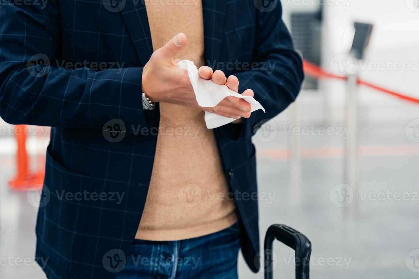 Keep your hands clean. Cropped shot of unrecognizable man disinfects hands with antibacterial napkin or antiseptic wet wipe during coronavirus spread, prevents virus, wants to be safe poses in airport photo