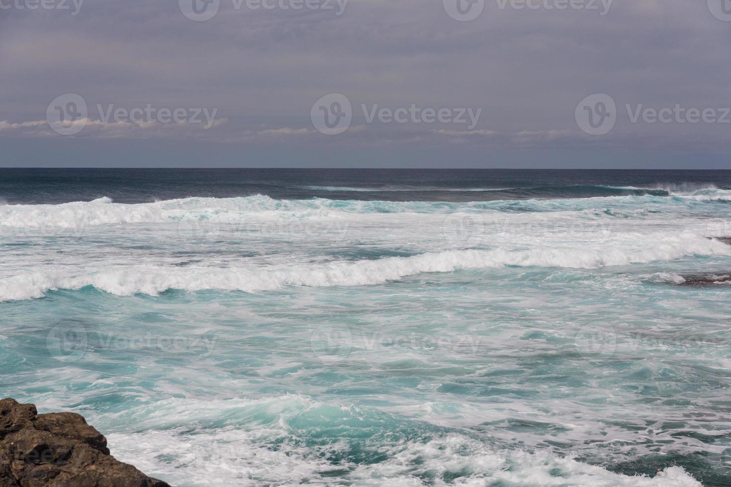 Turbulent ocean waves with white foam beat coastal stones photo