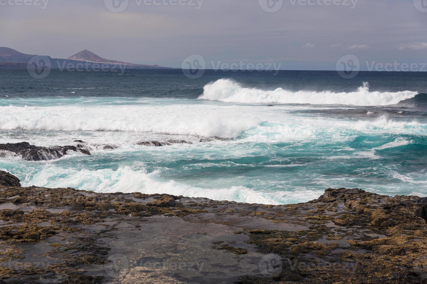 Las olas turbulentas del océano con espuma blanca golpean las piedras costeras. foto