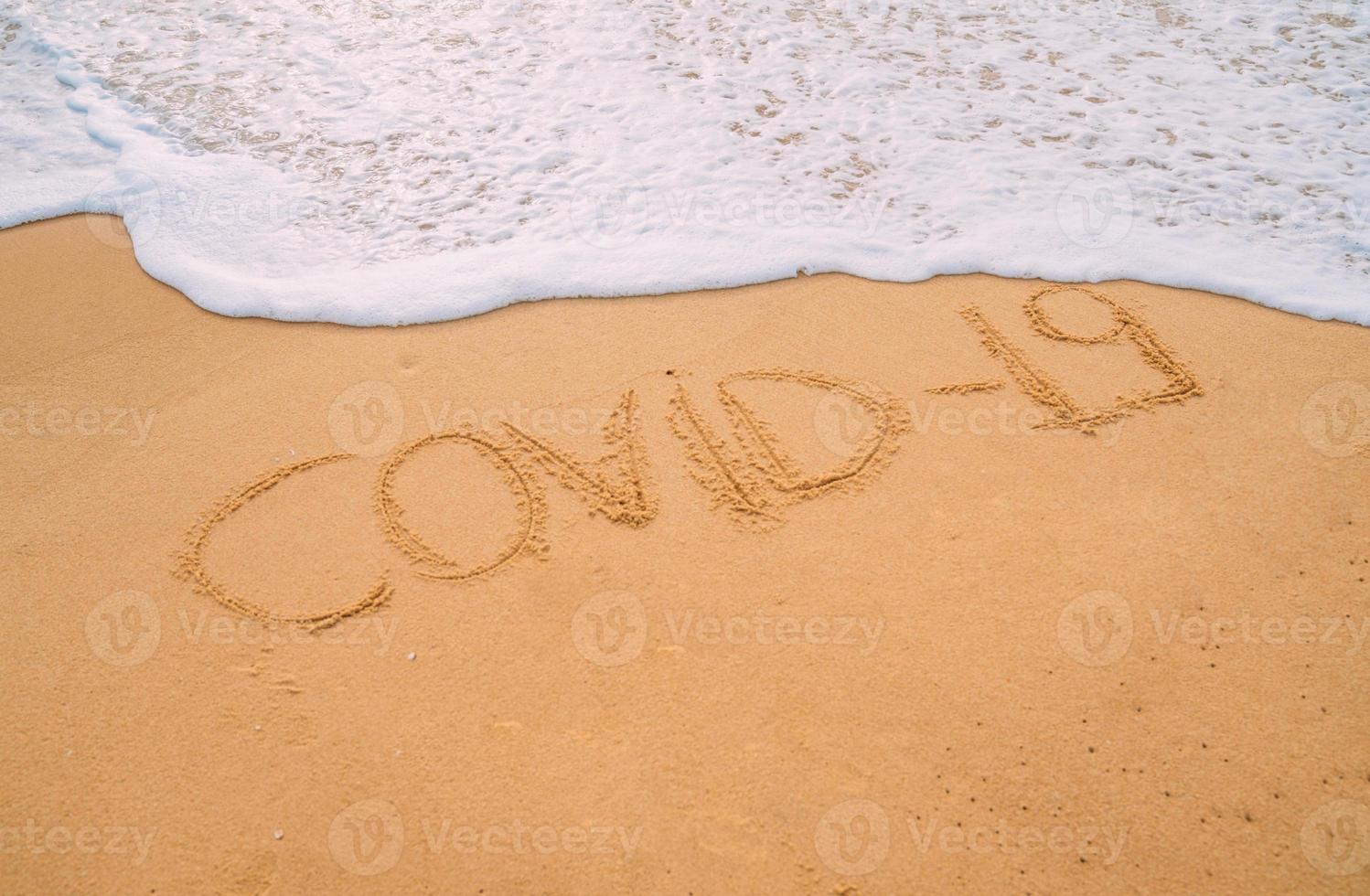 Closeup image of sea waves washing the word covid-19 from the sand on the beach. End of pandemic concept photo