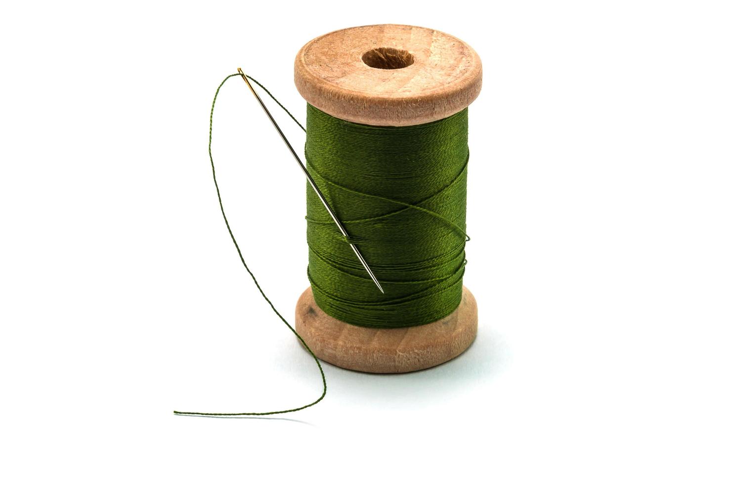 Isolated wooden spool of green thread with a needle photo