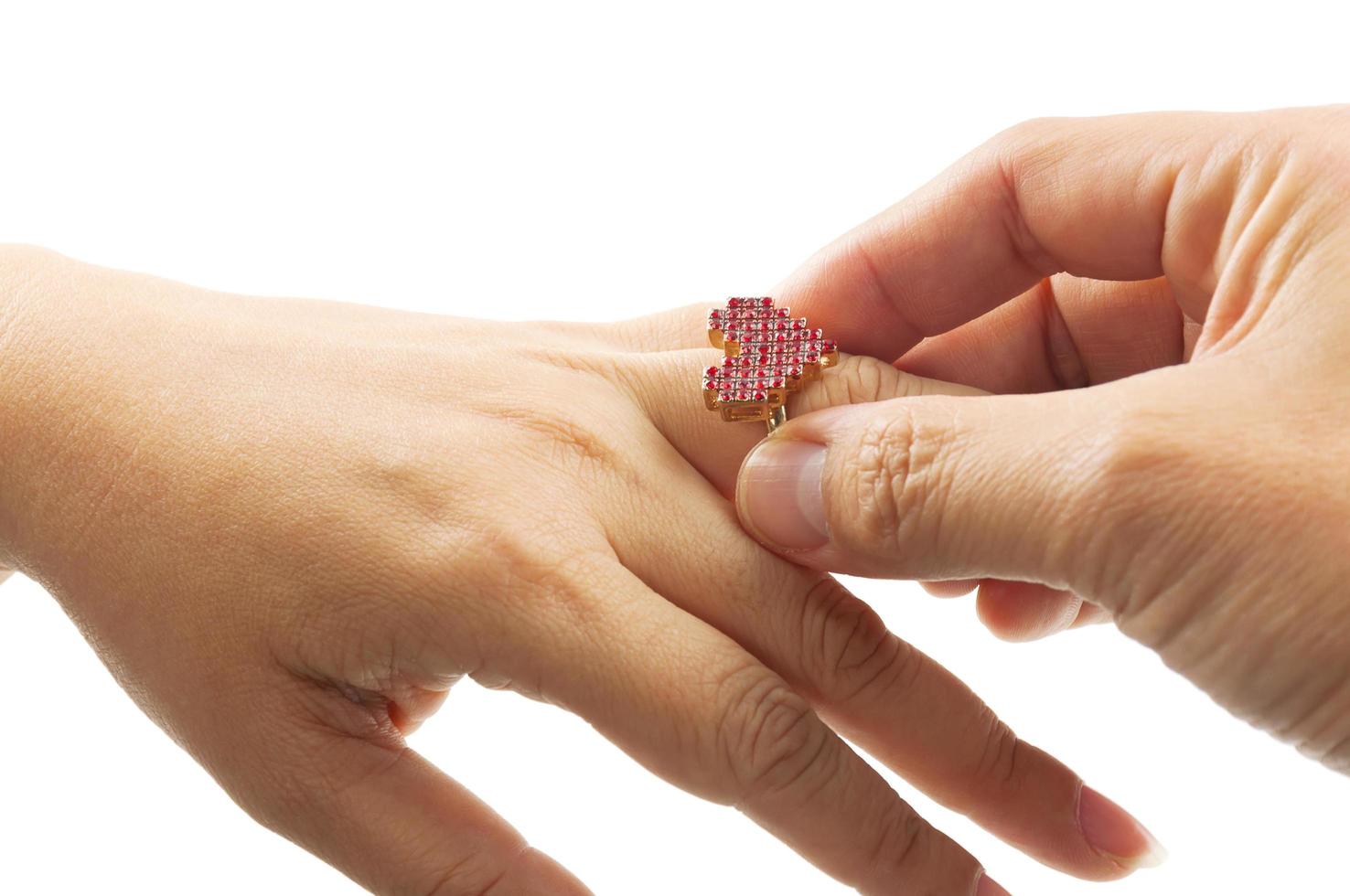 Close up of man's hand is putting heart shape ring to woman's ring finger over white background photo