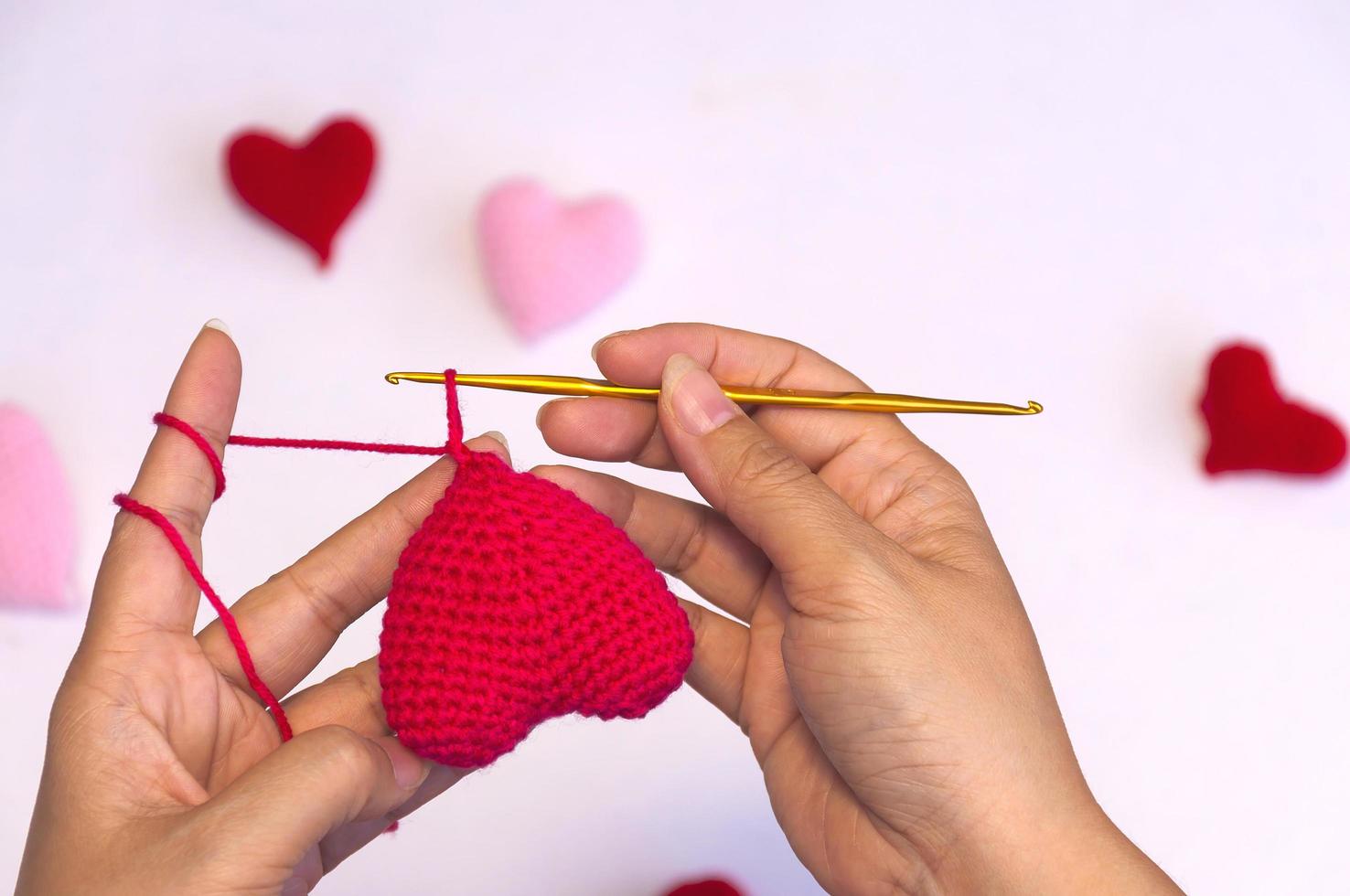 manos de dama haciendo trabajo de ganchillo haciendo forma de corazón rojo foto