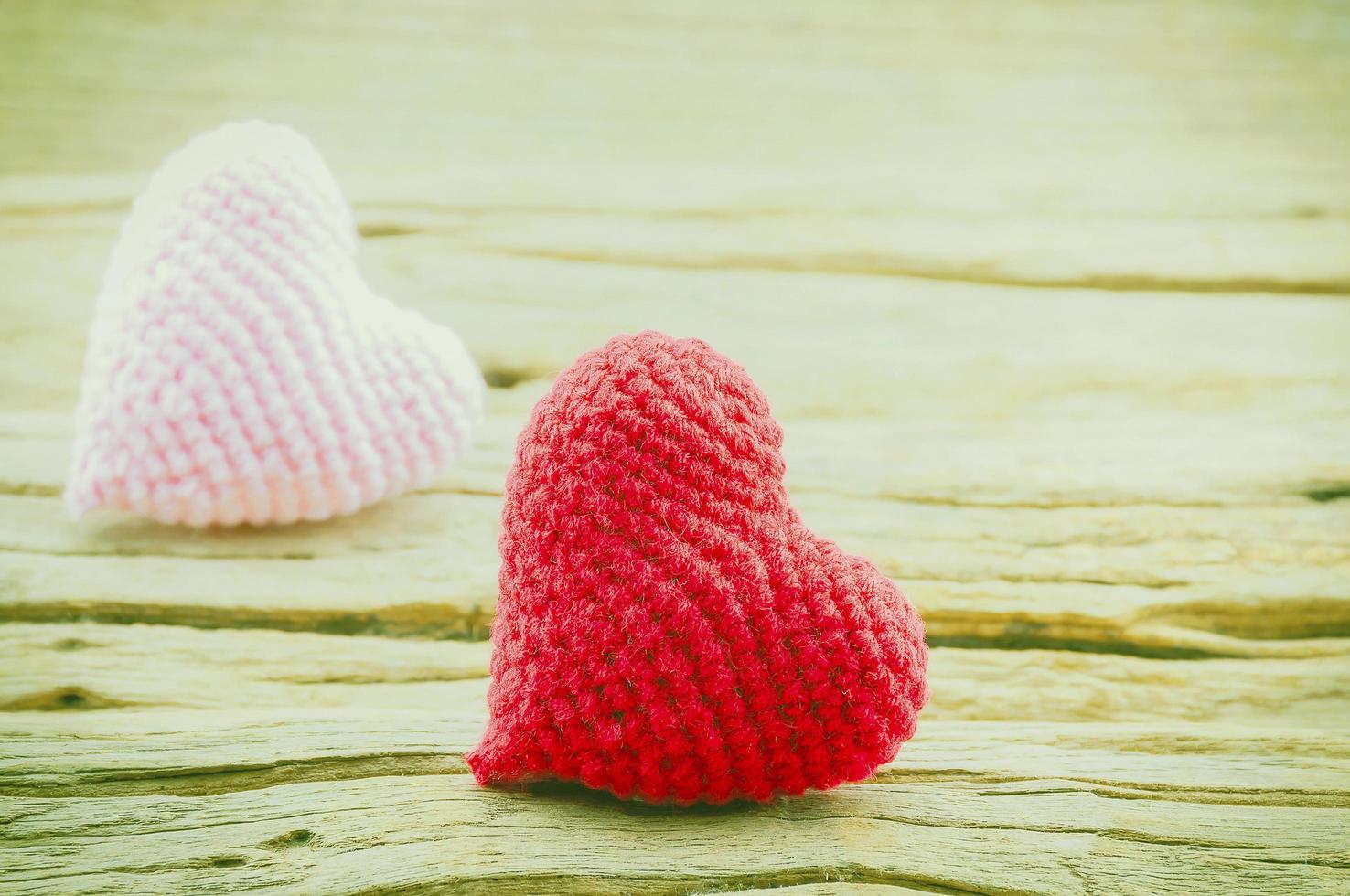 un par de corazones de ganchillo en rojo y rosa sobre fondo de madera. la foto se centra en el corazón rojo.