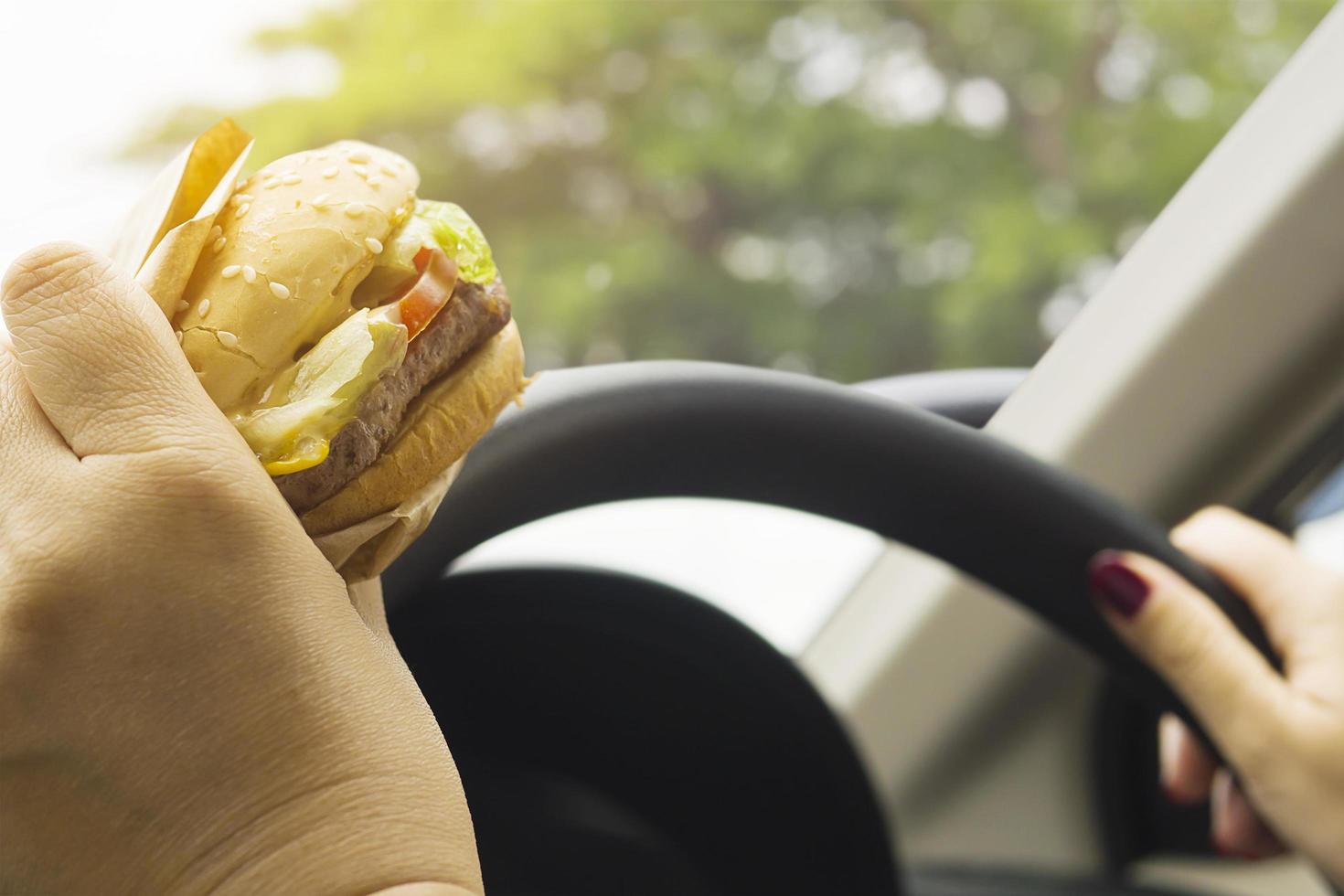Lady driving car while eating hamburger photo
