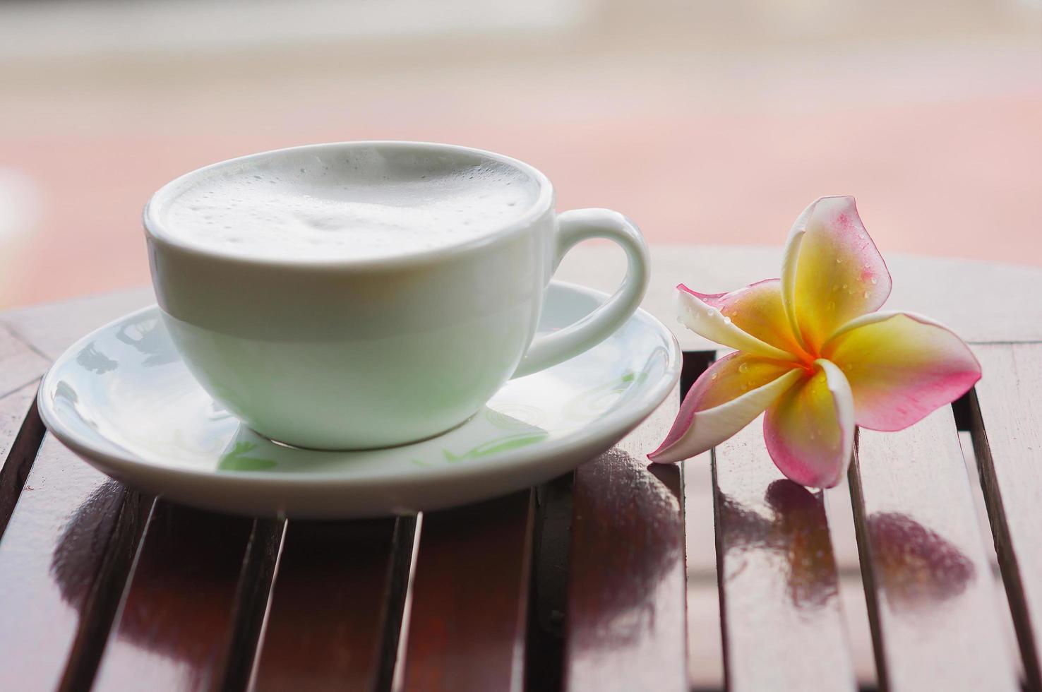 Plumeria flower with coffee cup on wooden table focusing at upper petal of plumeria. photo