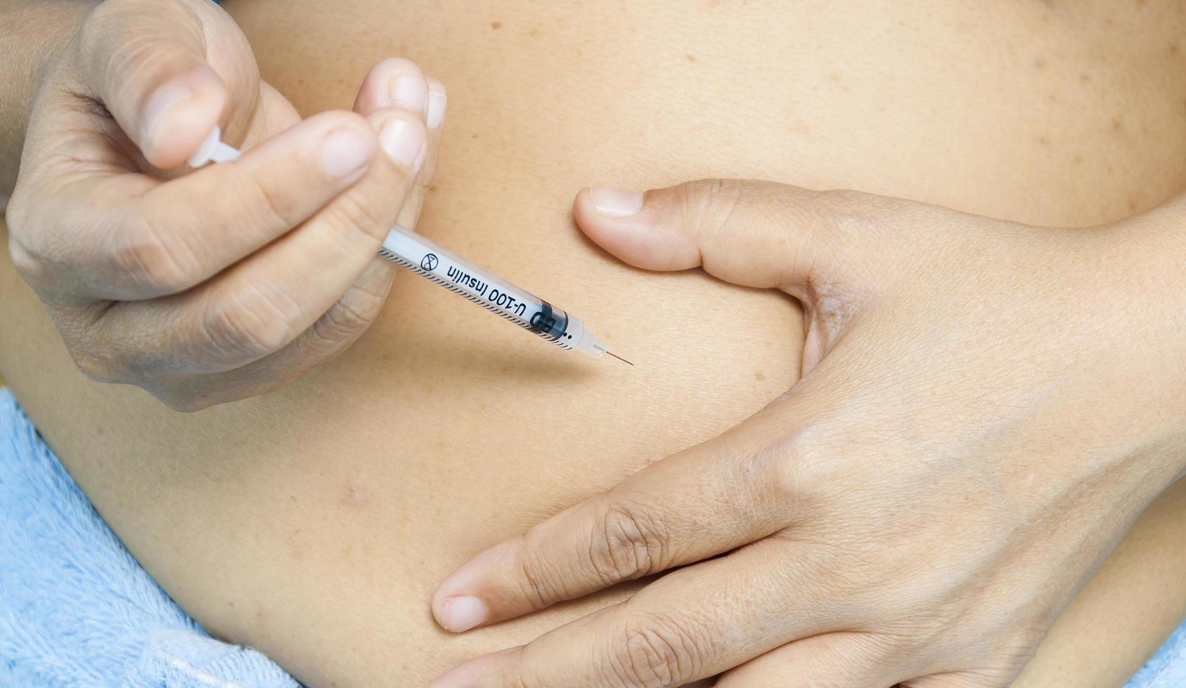 una señora se está inyectando insulina en el estómago. la foto está enfocada en la jeringa.