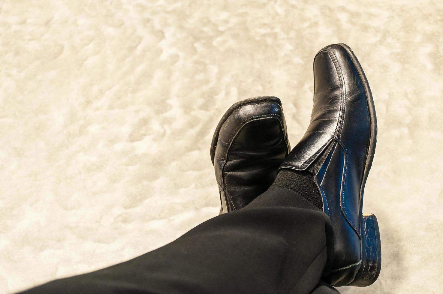 Top view of old black pants and leather shoes of relax sitting businessman on cement floor. Photo is focused at shoes.